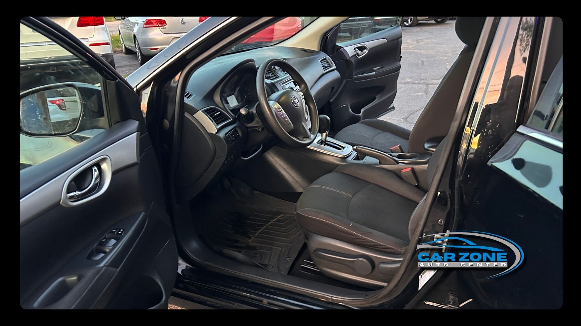 Car door open, showing a black leather driver’s seat and steering wheel inside a parked car.