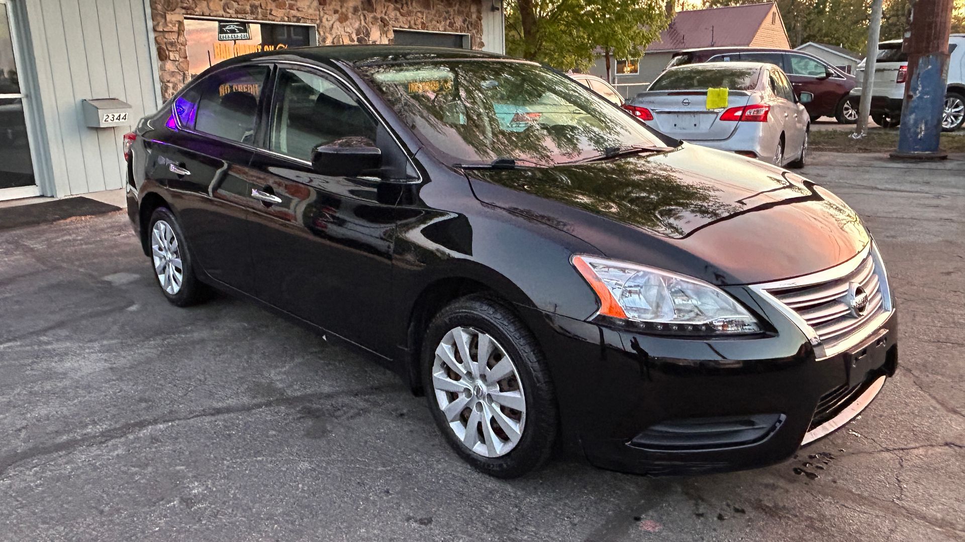 Black sedan parked in a driveway beside a house at dusk