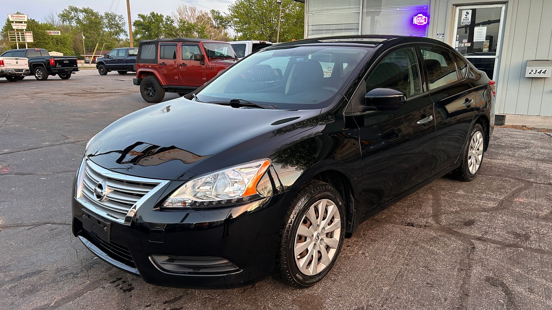 Black sedan parked in a lot beside a building, with a red SUV in the background.