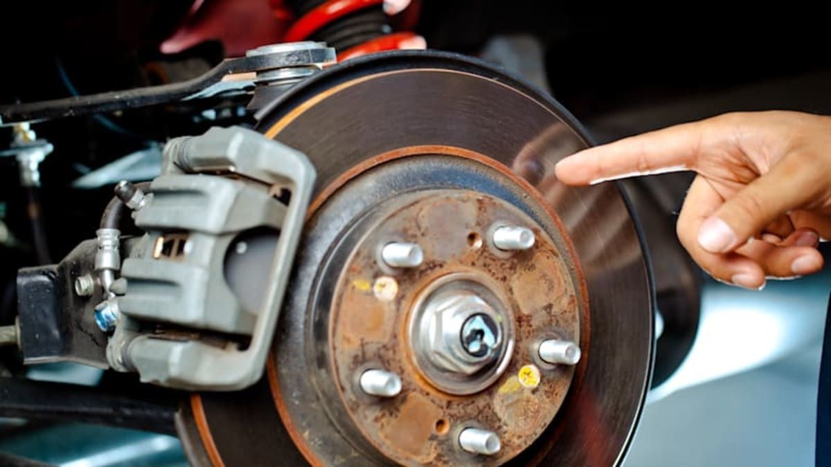 Hand pointing at a car brake rotor and caliper during inspection