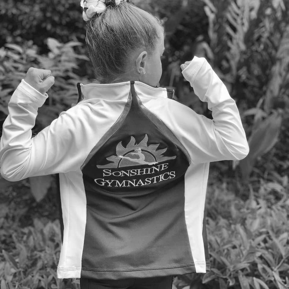 A black and white photo of a girl wearing a sunshine gymnastics jacket