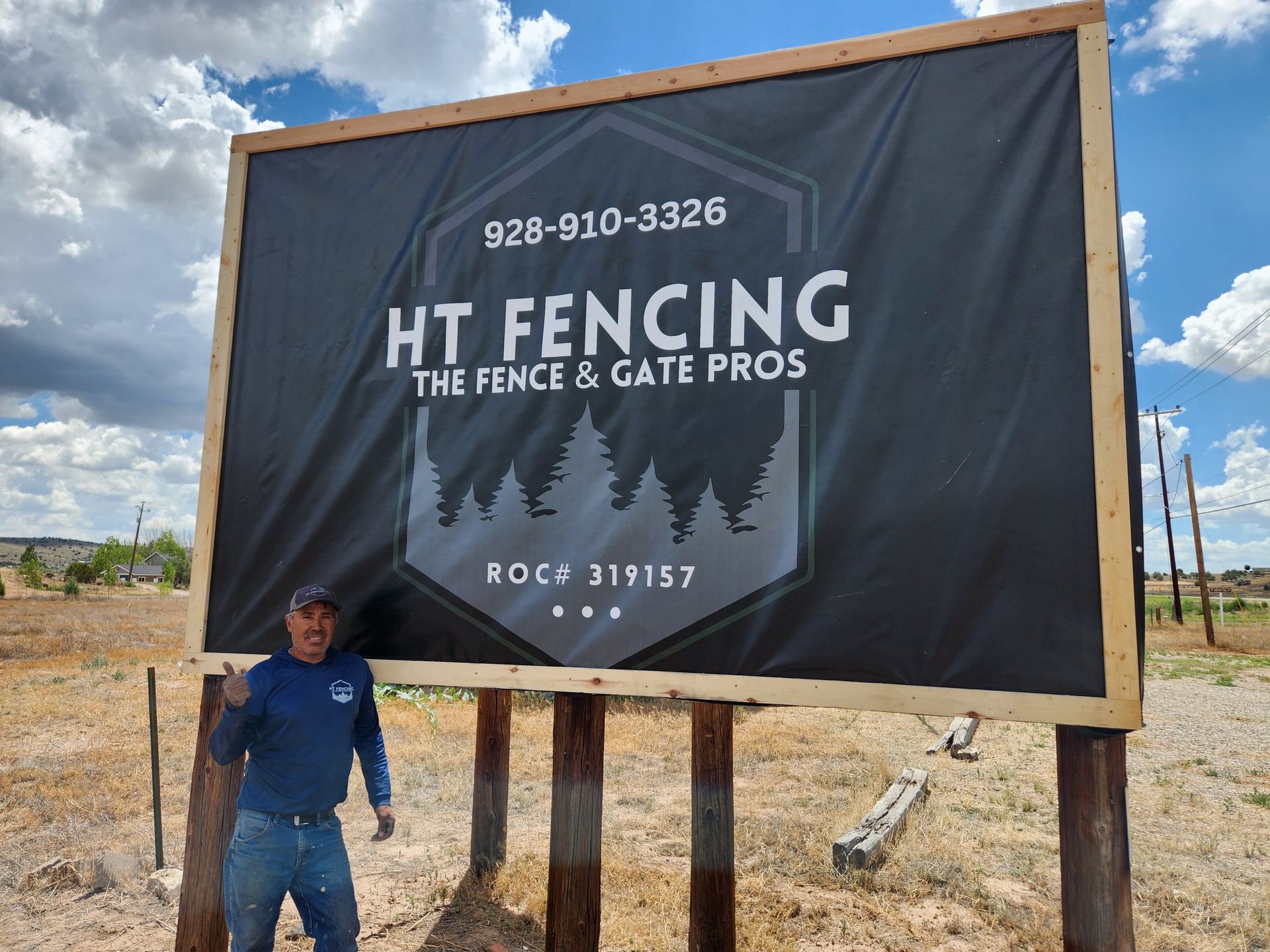 Man standing beside a large HT Fencing billboard under a cloudy sky