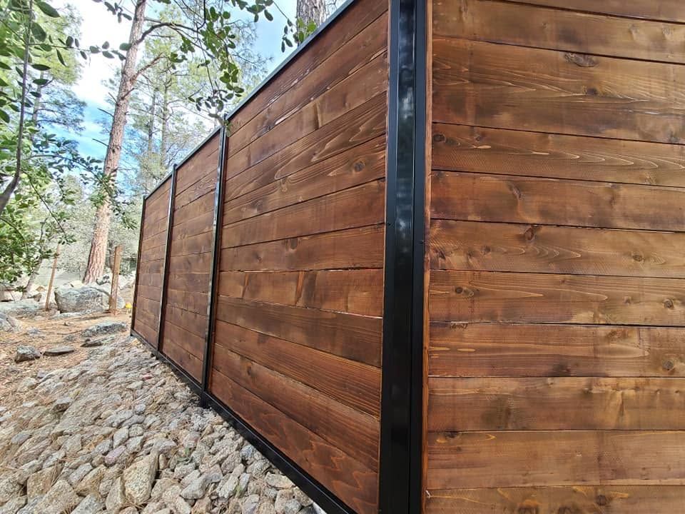 Tall wooden privacy fence with black metal posts along a rocky wooded hillside