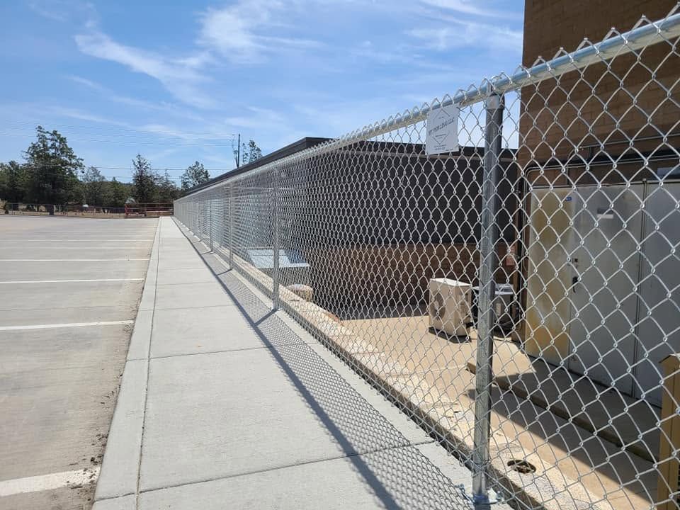 Chain-link fence along a sidewalk beside a parking lot and building under a clear sky