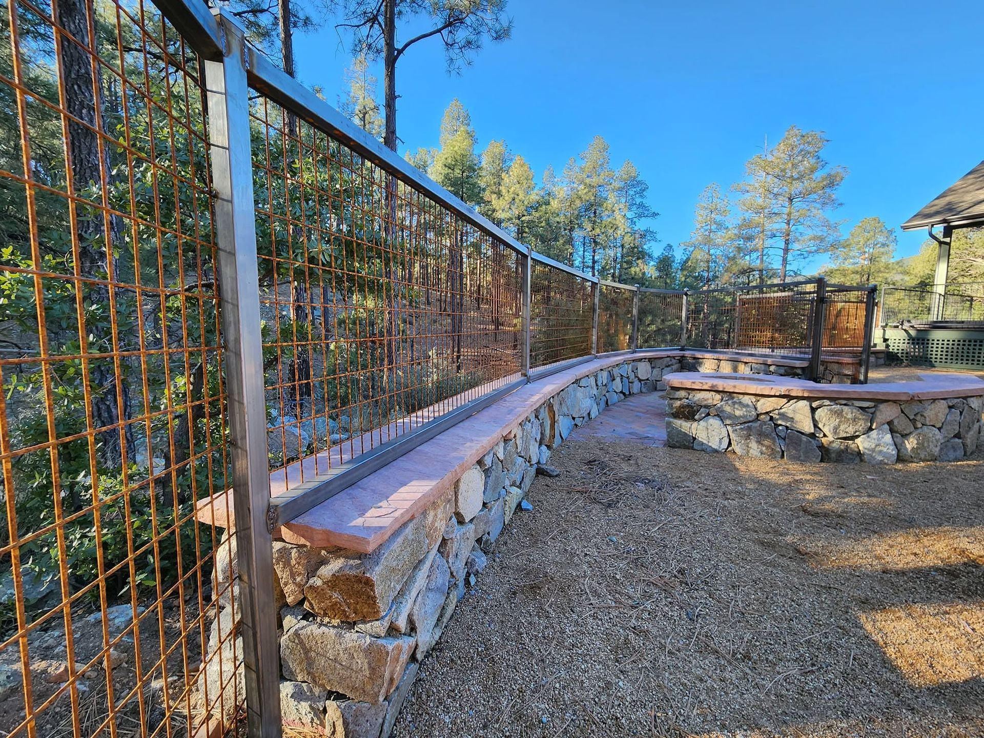 Curved stone bench and metal fence along a gravel path in a sunny wooded park