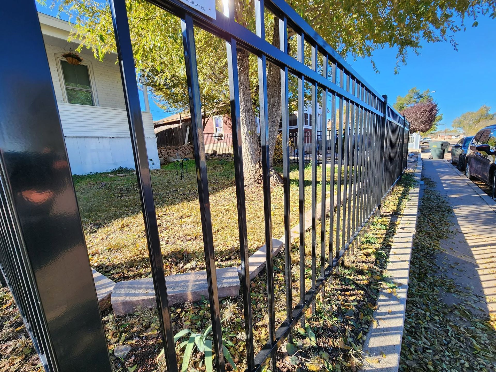 Black metal fence along a sidewalk beside a grassy yard and house on a sunny day