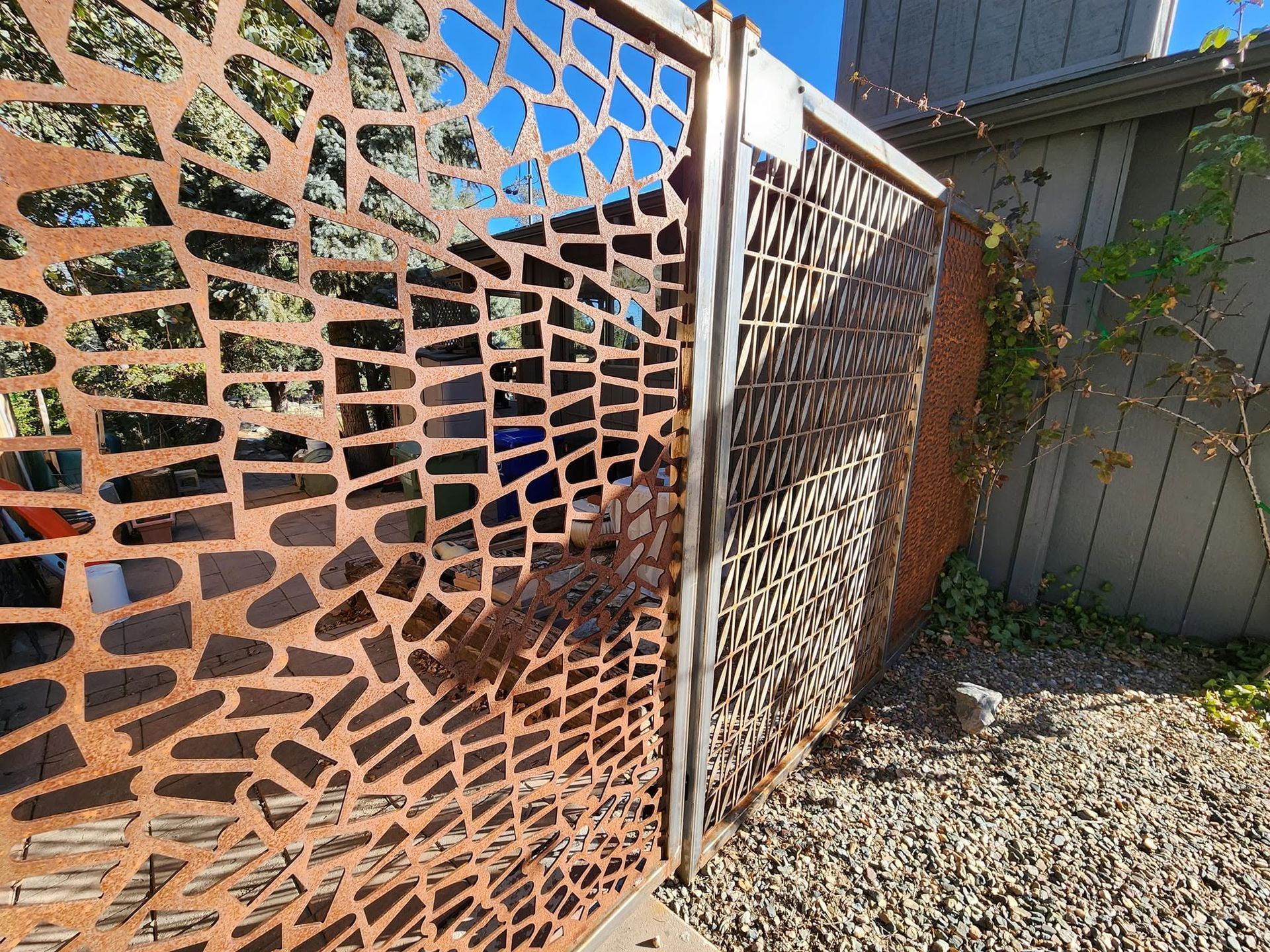 Rusty metal privacy screen beside a lattice fence in a gravel backyard