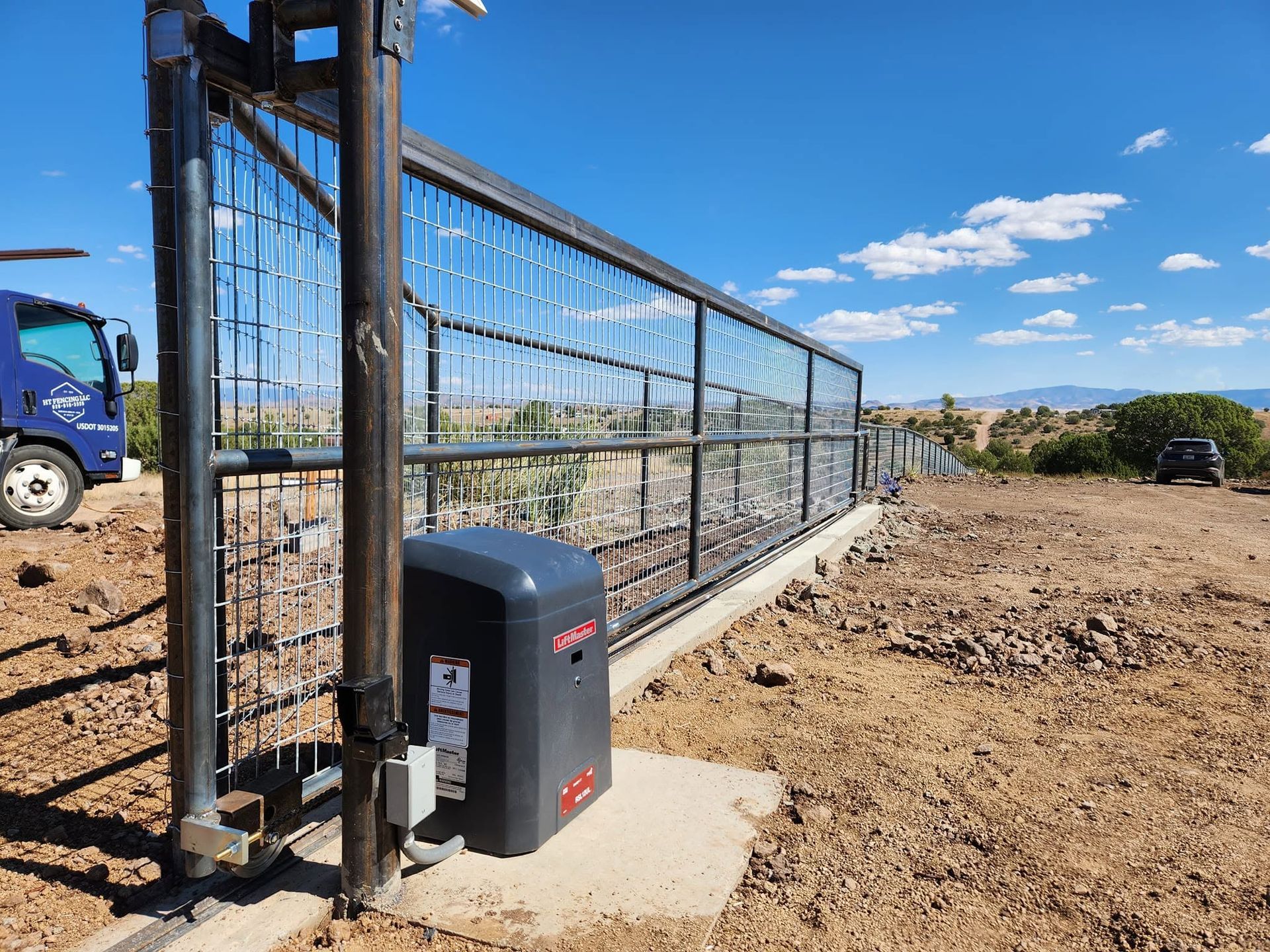 Black metal sliding gate with motor on a dirt driveway under a blue sky at a construction site