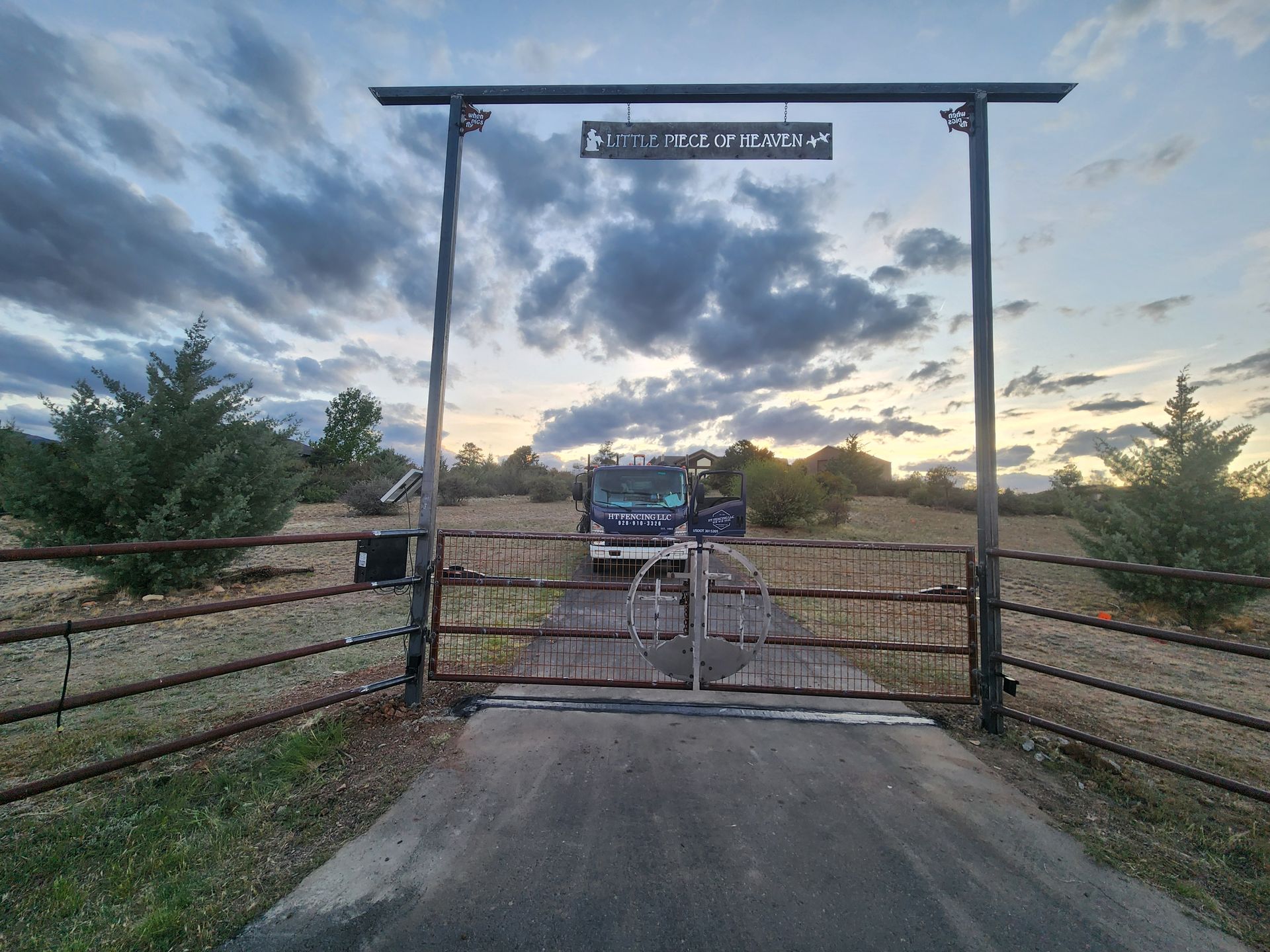 Gated ranch entrance with a truck beyond the open gate at sunset under a cloudy sky
