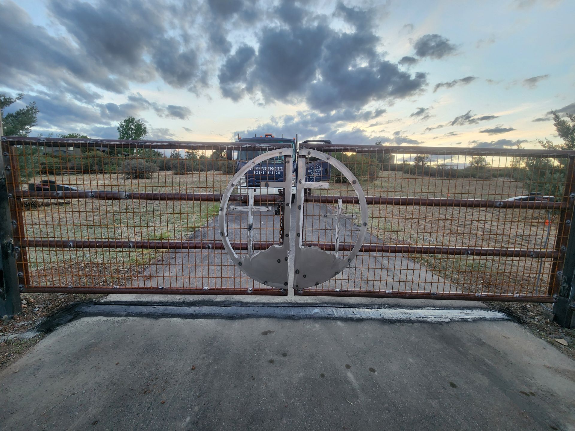 Closed metal gate at a rural property entrance under a cloudy sunset sky