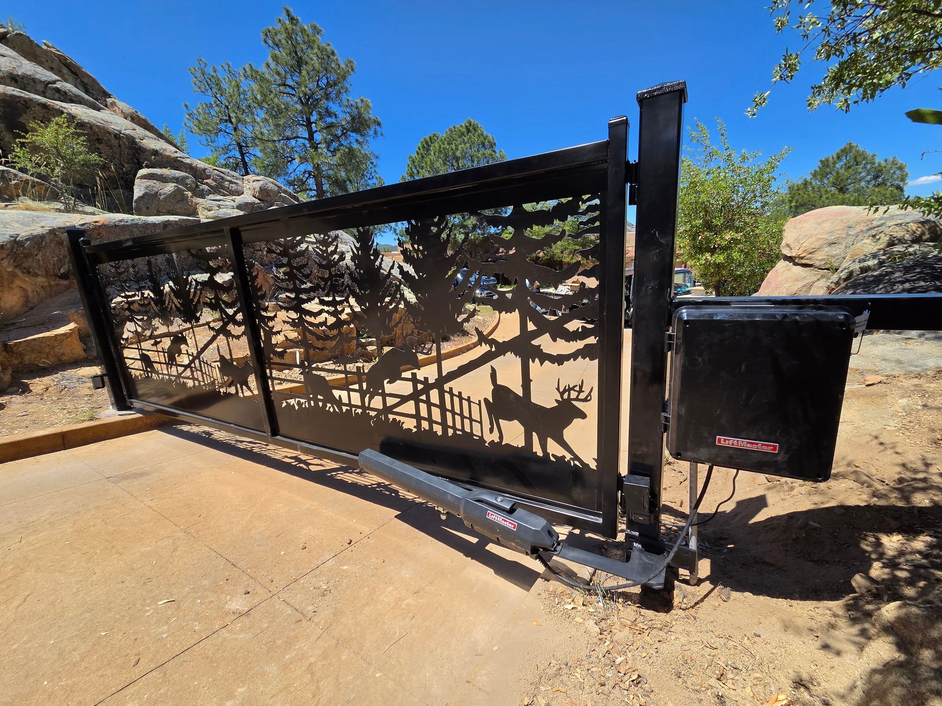 Black metal ranch gate beside a dirt path, with desert rocks and blue sky in the background