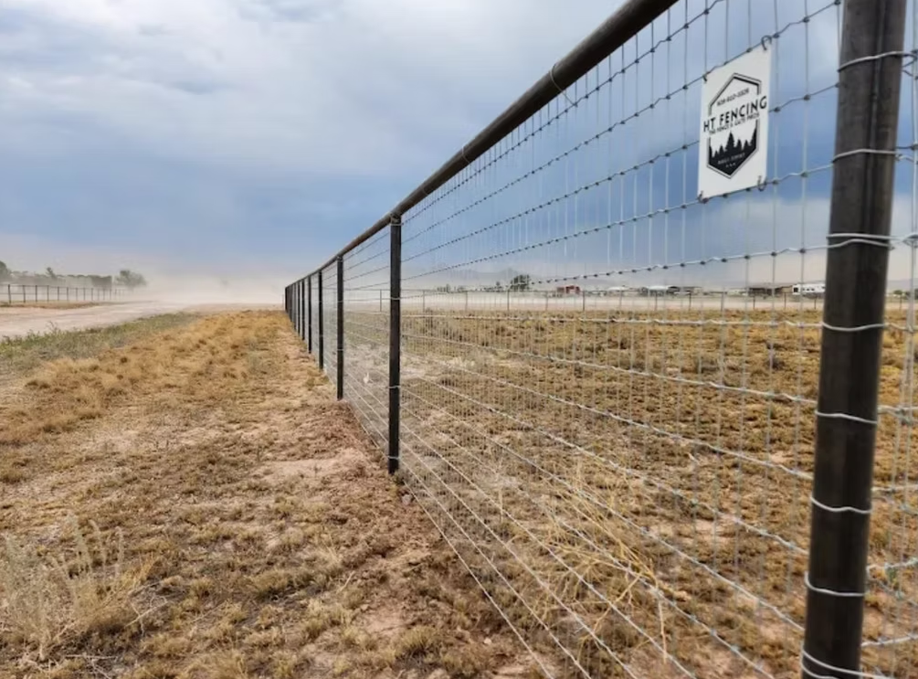 Wire fence along a sandy shoreline under a cloudy sky, with a small sign on the fence