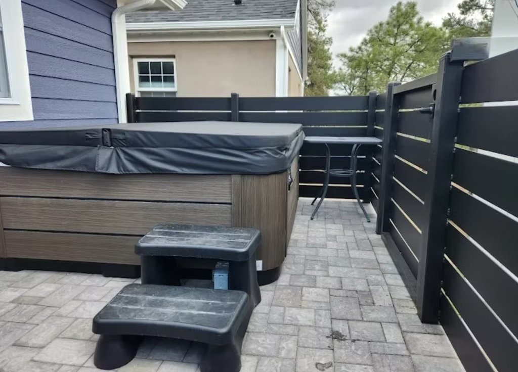 Backyard patio with hot tub, black fencing, and stone pavers leading to a house