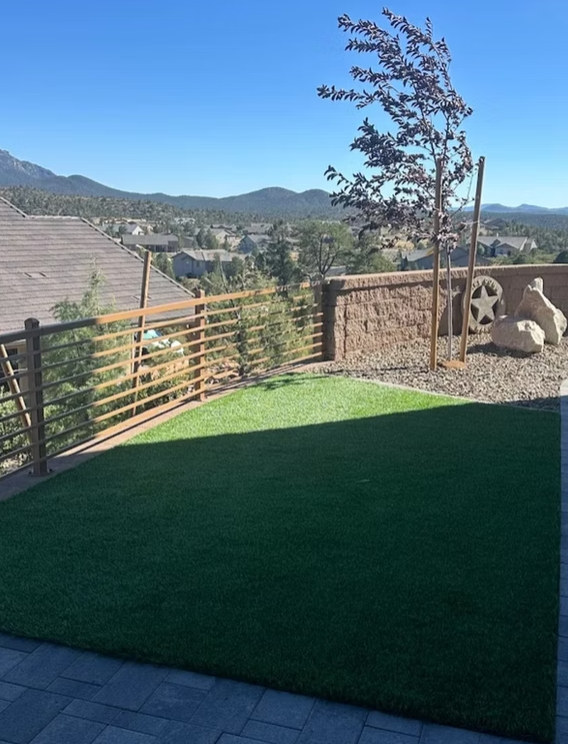 Patio with artificial grass, stone wall, tree, and mountain view under a clear blue sky
