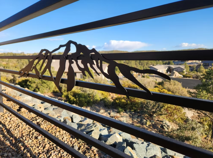 Metal dinosaur sculpture on a bridge railing overlooking a rocky desert landscape under a blue sky