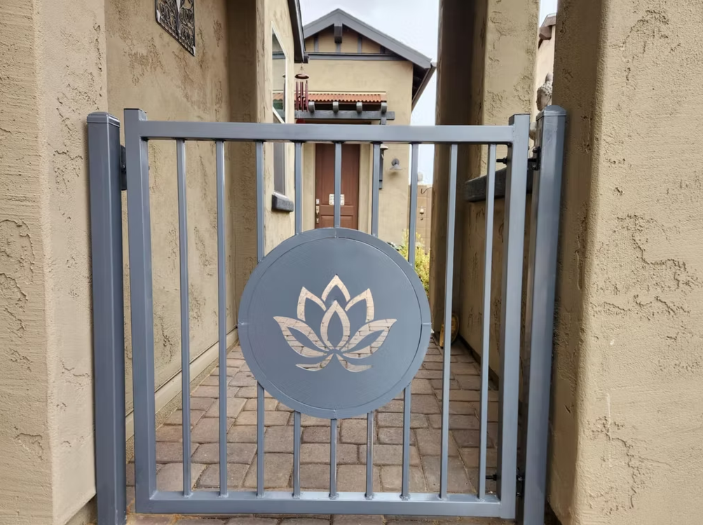Gray metal gate with a circular lotus emblem in a narrow outdoor alley between stucco walls