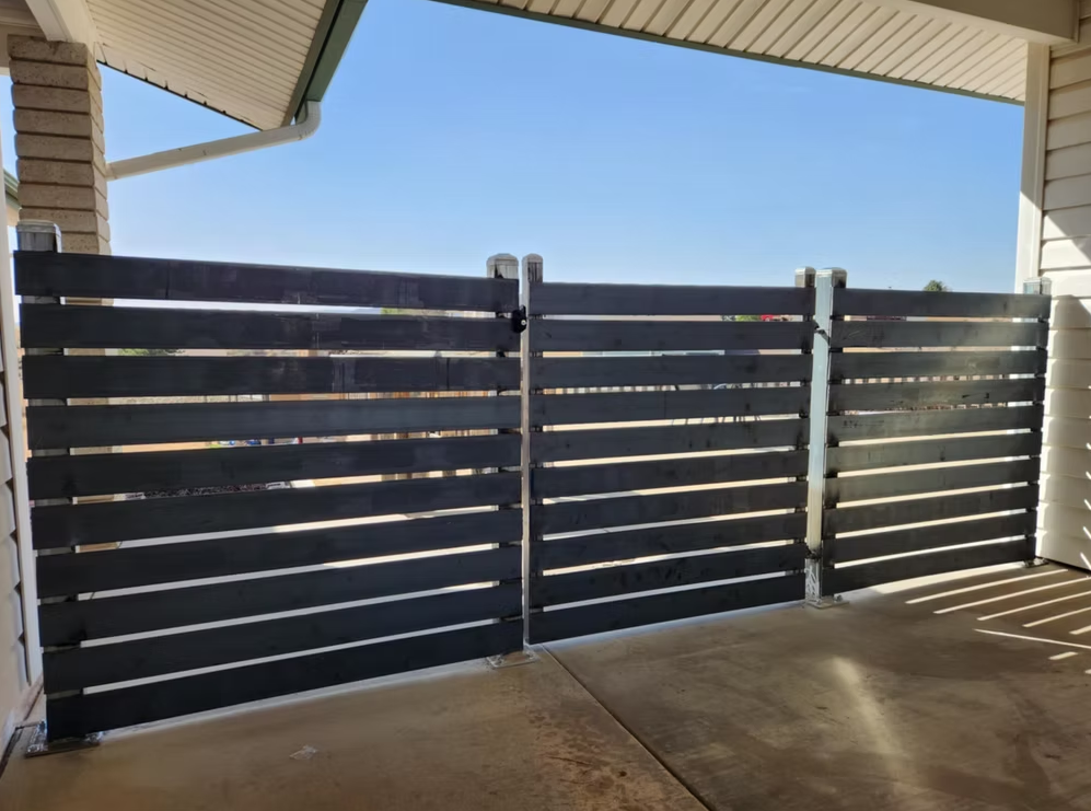 Covered patio with dark horizontal slat fence and blue sky beyond