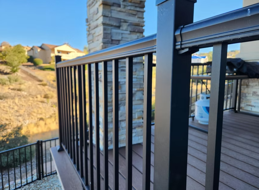 Balcony railing beside a deck, overlooking a rocky hillside and nearby buildings at sunset