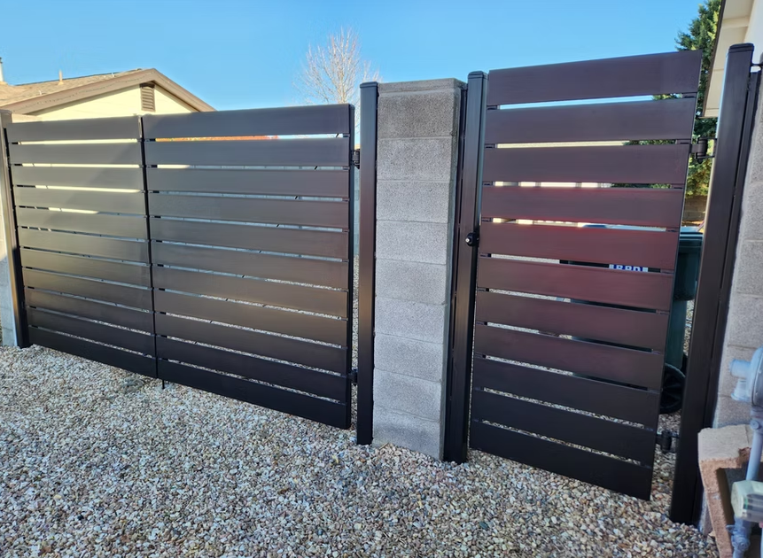 Modern black slat gate with a gray stone pillar beside a gravel driveway