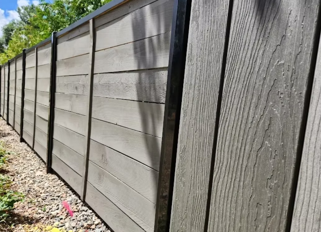 Long gray wooden fence along a gravel path under a blue sky