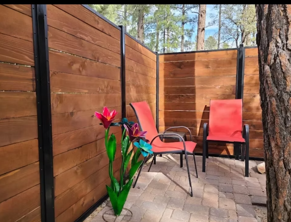 Patio with two red chairs, potted flowers, wood fence, and a tree in a sunny outdoor setting