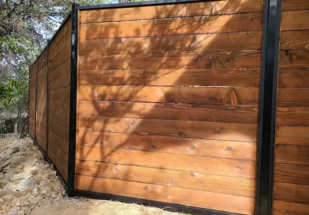 Wooden privacy fence with dark support posts in a dry outdoor area, casting tree shadows