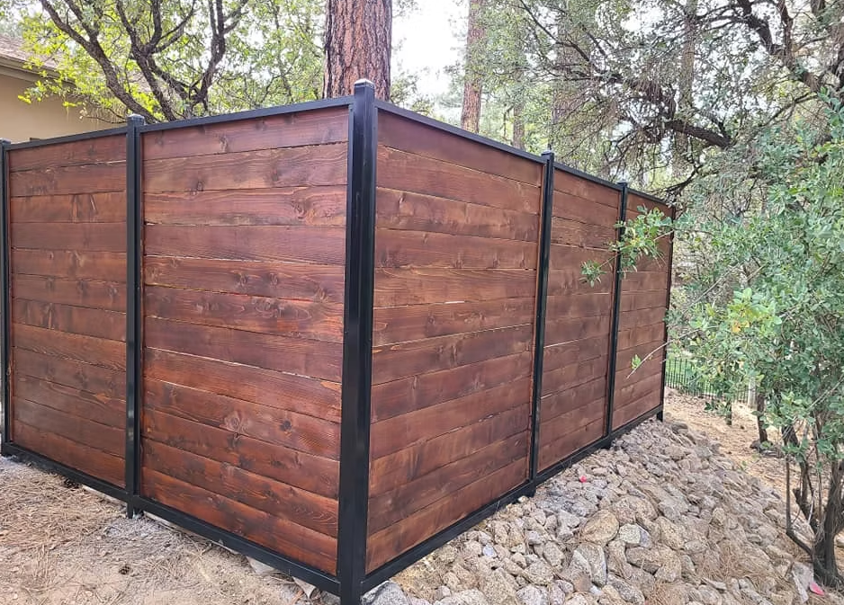 Wooden privacy fence with black metal trim in a wooded outdoor area