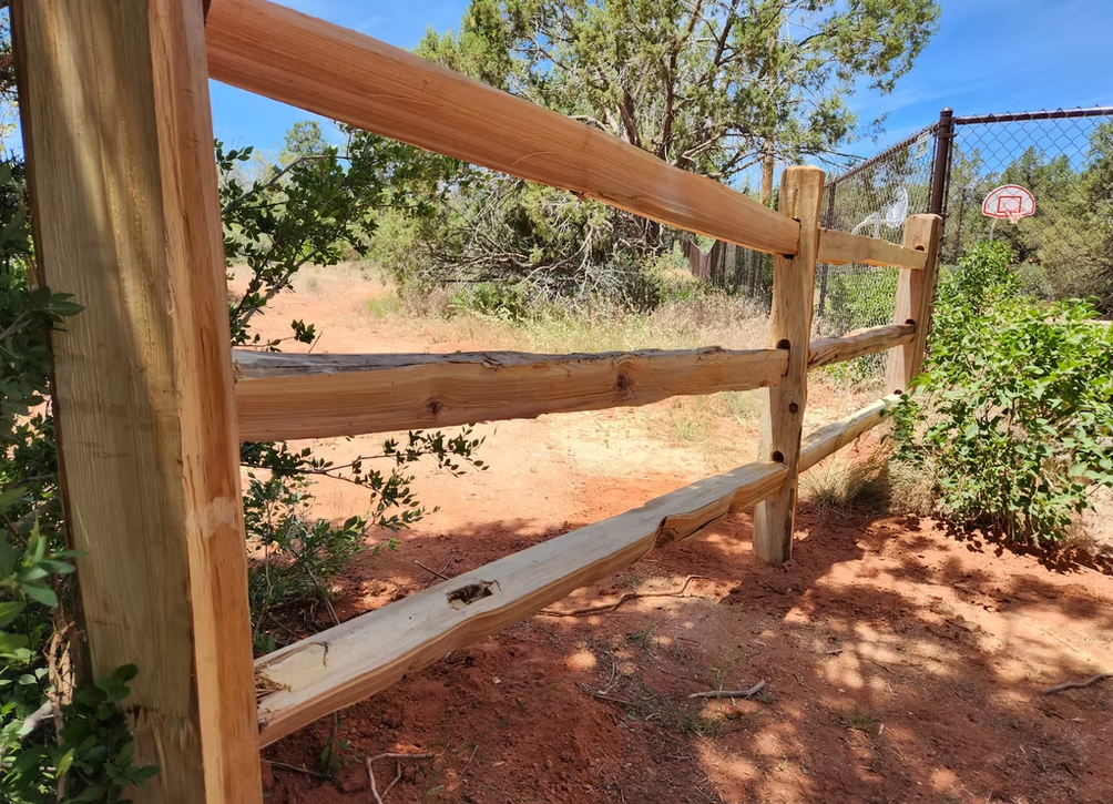 Wooden fence beside a dirt path, with dry brush and trees in the background.