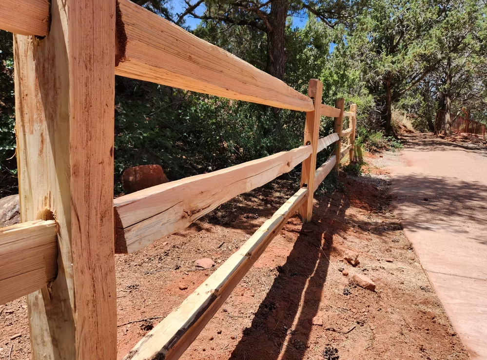 Wooden fence lining a dirt trail through a sunlit wooded area