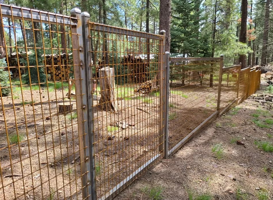 Wire fence with gate in a wooded outdoor area and dirt ground