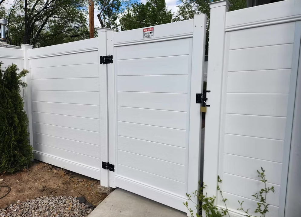 White vinyl gate and fence with black hinges beside a gravel walkway and greenery