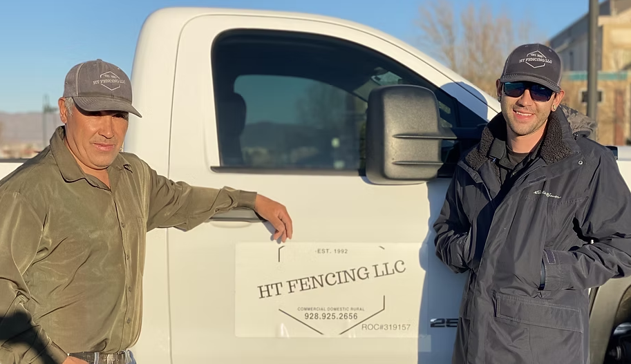 Two men standing beside a white RT Fencing LLC truck on a sunny day.