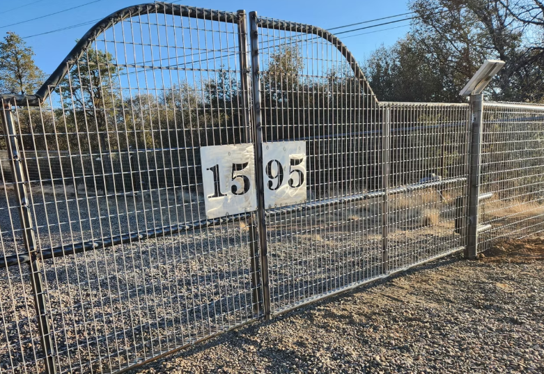 Chain-link gate with large house number signs “1595” in front of a yard and arched structure