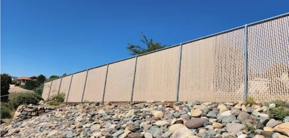 Concrete sound barrier wall above rocky slope under a clear blue sky