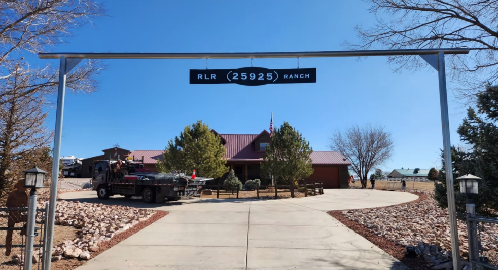 Entrance drive to a building with a blue sky, bare trees, parked cars, and a curved walkway