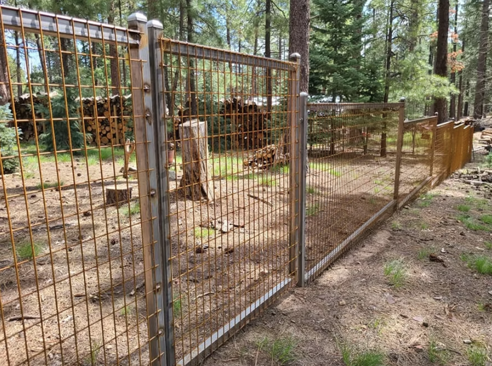 Wire mesh fence enclosing a wooded animal enclosure with metal posts and a dirt ground