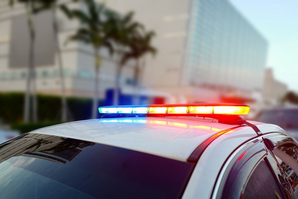 Police car with flashing red and blue lights atop, in front of a building.