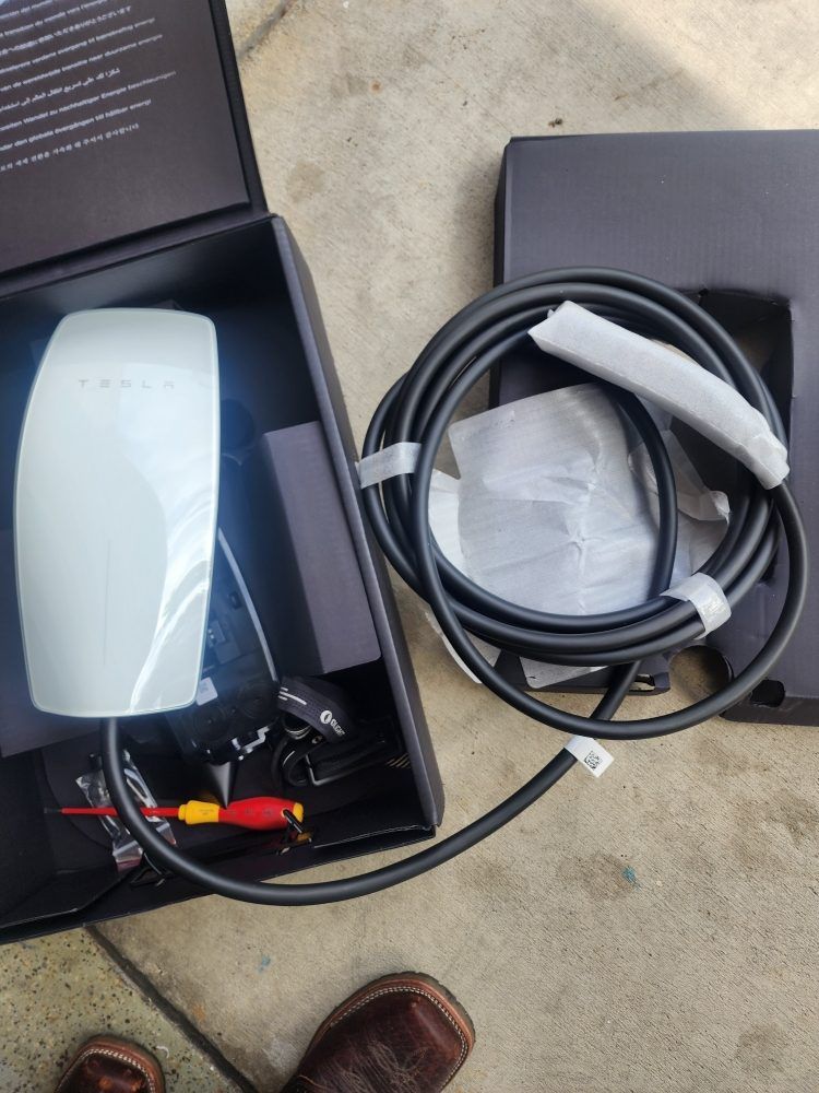Open case with white device, cables, and accessories beside a black box on concrete floor.