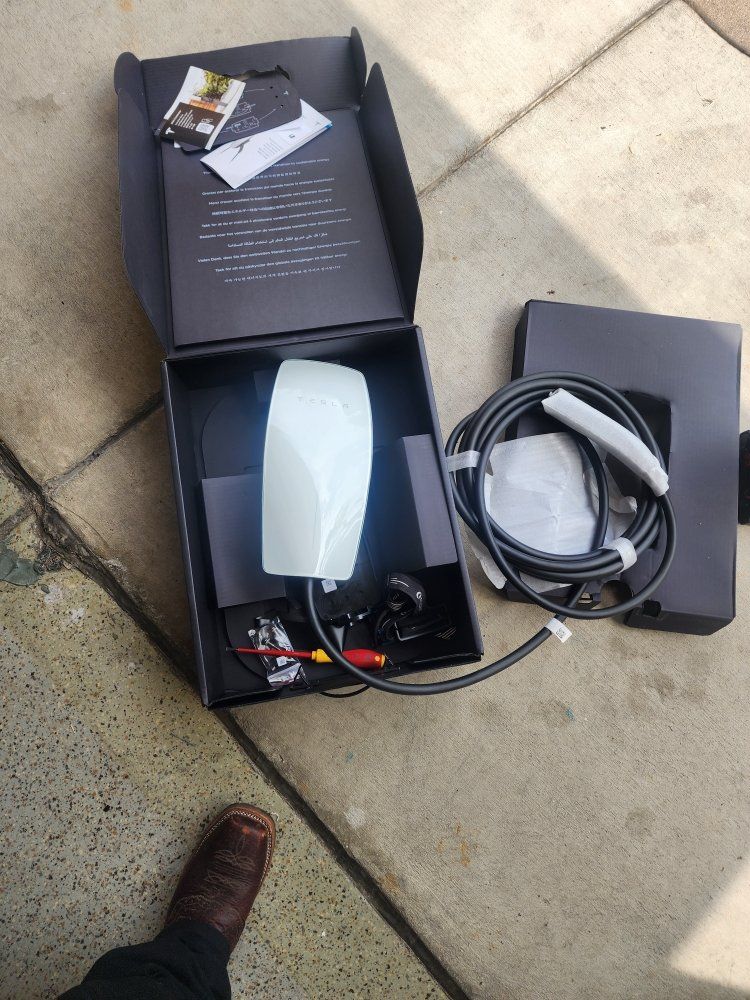 Open box with a small device, cables, and accessories on outdoor pavement.