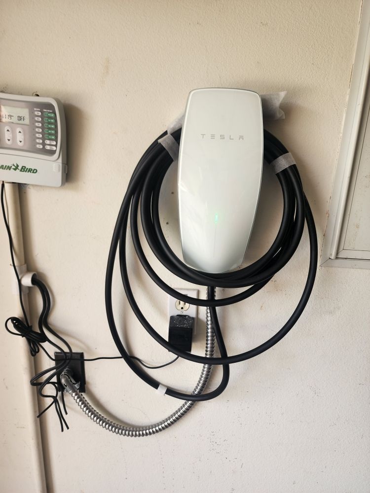 Wall-mounted EV charger with coiled cable beside a small control panel on an indoor wall