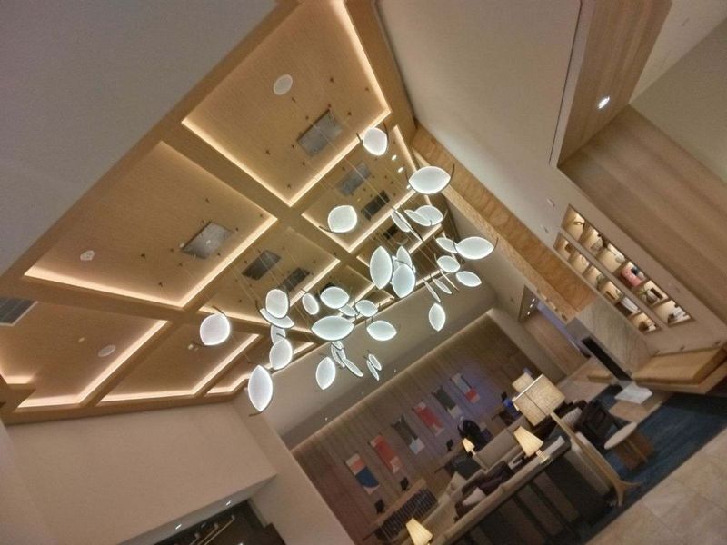 Modern lounge ceiling with geometric wood panels, pendant lights, and seating area below