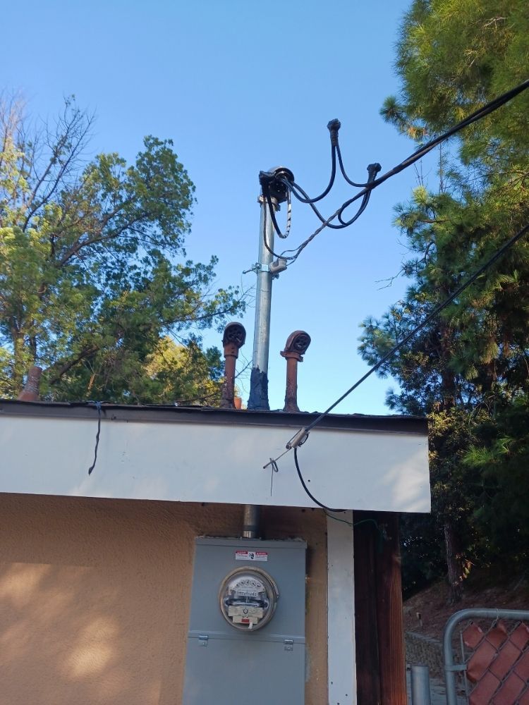 Utility meter and overhead cables on a house roof against a blue sky and trees