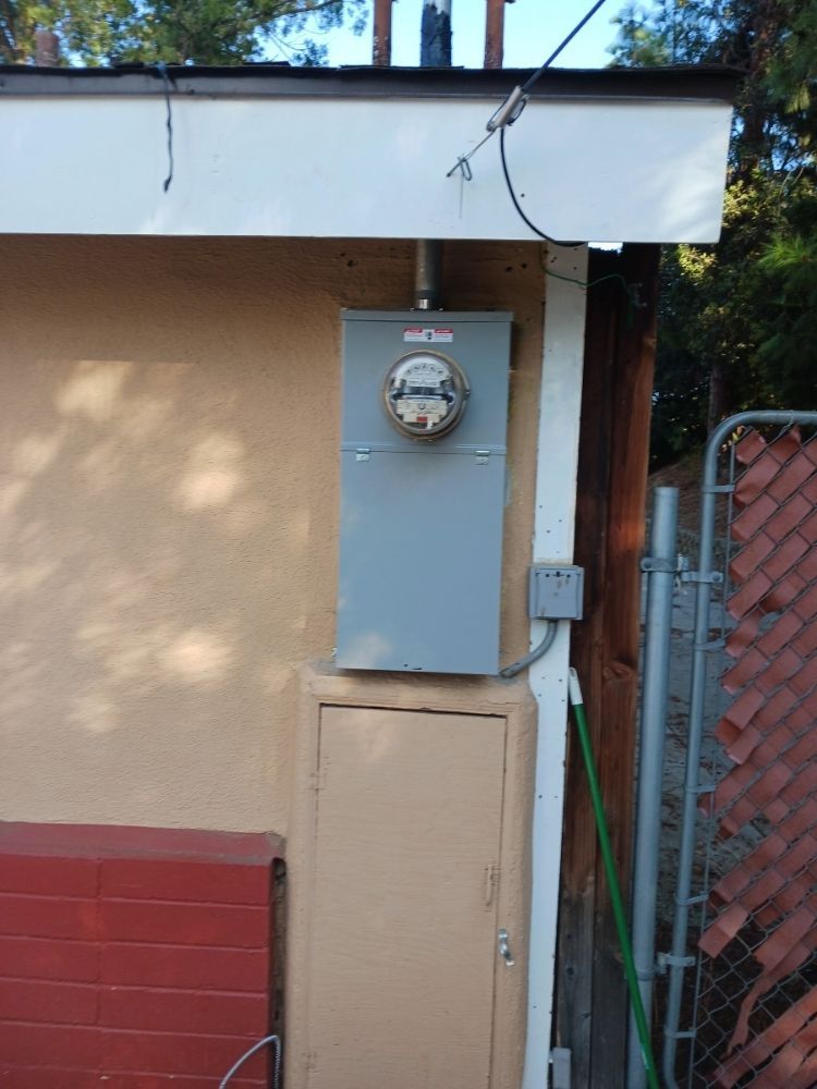 Outdoor electrical meters mounted on a beige wall beside a red fence and small utility box