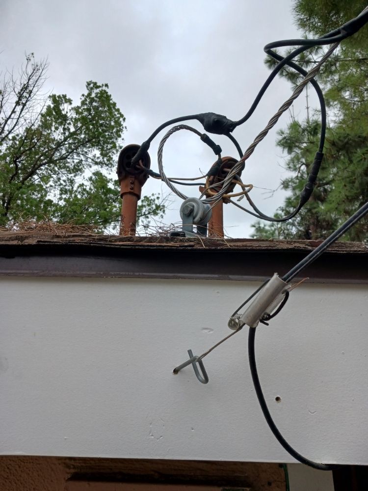 Electrical cables and rooftop equipment above a white wall, with trees in the background.