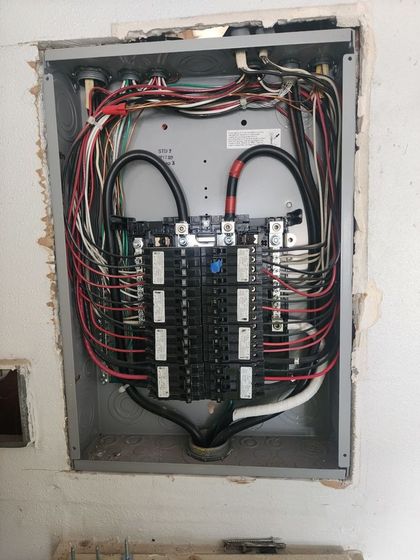 Open electrical breaker panel with wiring and circuit breakers mounted in a wall recess