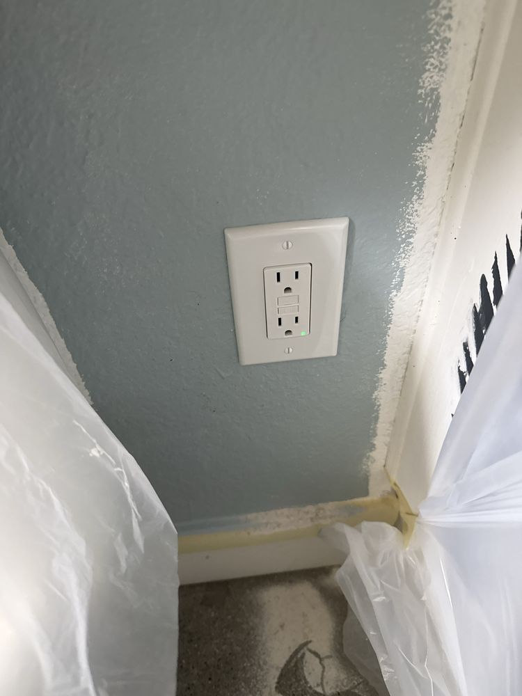 Electrical outlet on a gray wall beside a covered floor and white plastic sheeting during painting or renovation