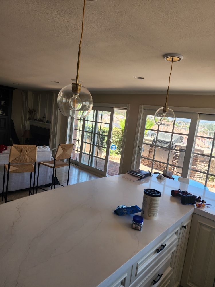 Bright kitchen with white island, pendant lights, and large windows overlooking a patio.