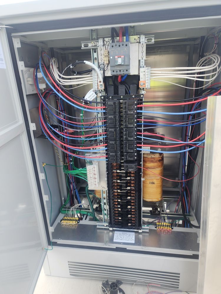 Open electrical control panel with multicolored wiring and circuit components inside a gray cabinet