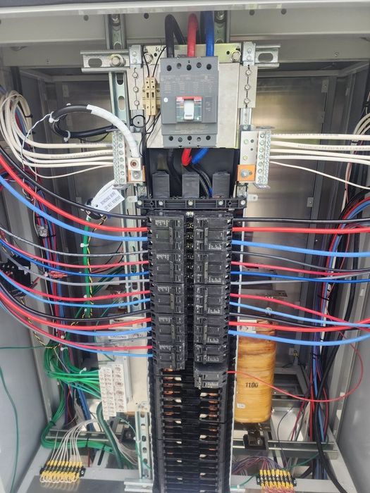 Open electrical panel with wires, breakers, and control components inside a metal cabinet.