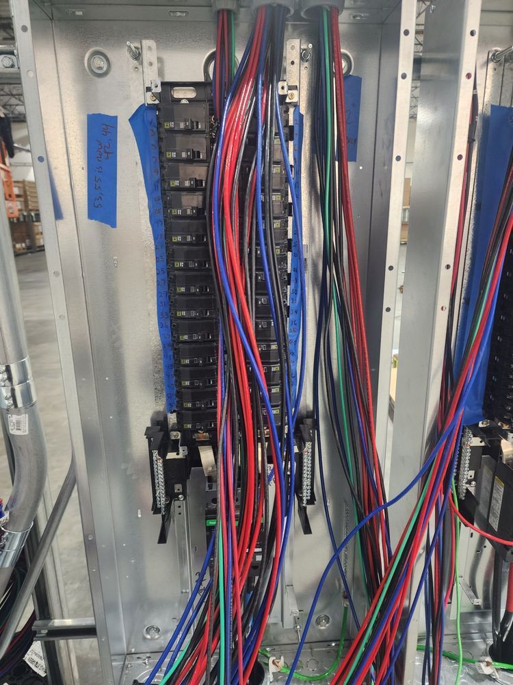 Electrical panel with dense red, blue, and black wiring inside an open cabinet.